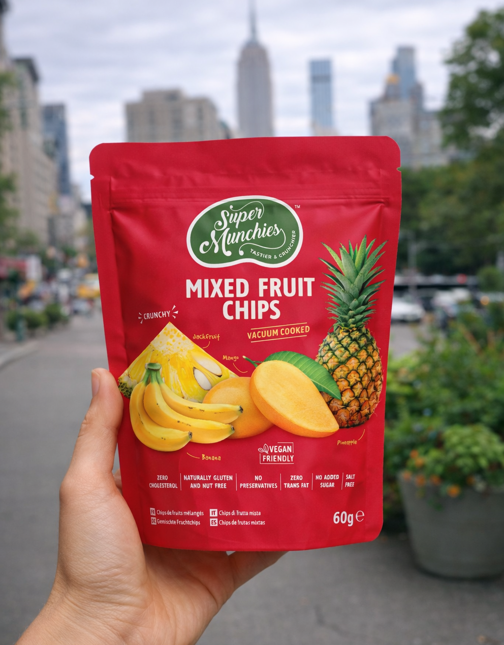 Opakowanie Mixed Fruit Chips Super Munchies trzymane w dłoni na tle miasta, naturalnie słodkie i chrupiące chipsy z mango, ananasa, banana i jackfruita